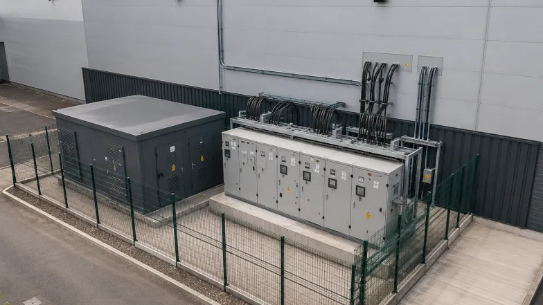 Substation kiosk and switchgear cabinets behind mesh fencing at a building's supply intake